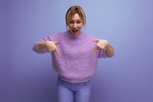 portrait of joyful cute blondie woman in lavender sweater showing hand down on purple background with copy space.