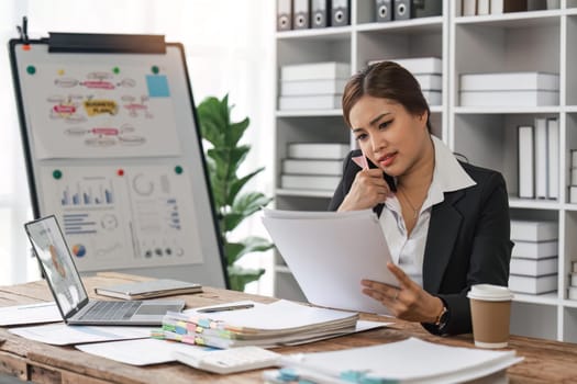 business woman sitting at office desk in front of laptop hold mobile phone make pleasant business or informal call. Successful businessman looking at financial statistic shown on documents.