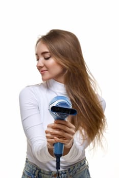 Portrait of attractive cheerful girl drying long hair. focus on hair dryer
