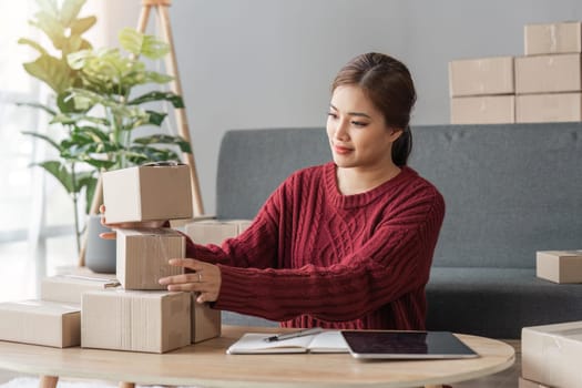 Happy young asian woman startup small business freelance holding parcel box and computer laptop and sitting sofa, Online marketing packing box delivery concept.