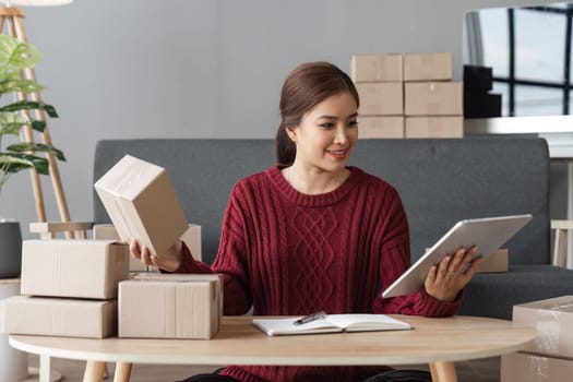 Asian woman holding parcel boxes and holding laptop, she owns an online store. Online selling concept.