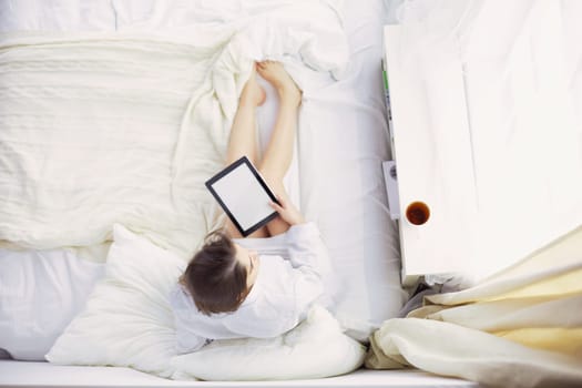Portrait of woman using tablet and drinking coffee while sitting on the bed in the morning.