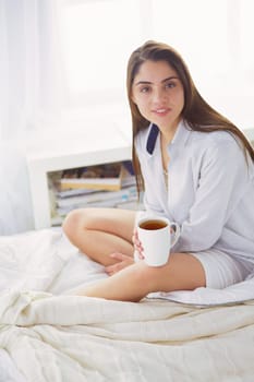 Woman sitting in bed reading a book and having breakfast.