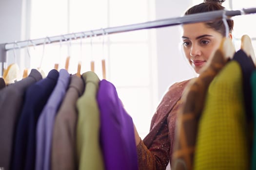 Beautiful young stylist near rack with hangers.