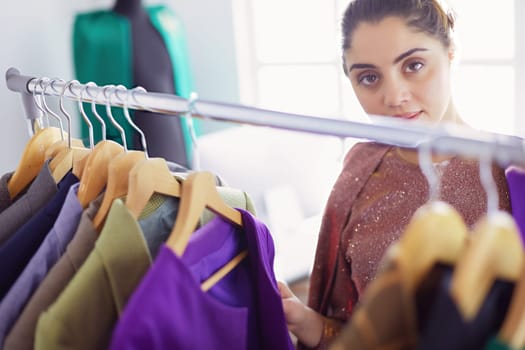 Beautiful young stylist near rack with hangers.