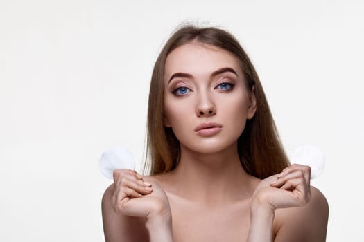 adorable woman holding two white cotton disks pad with micellar water on white background