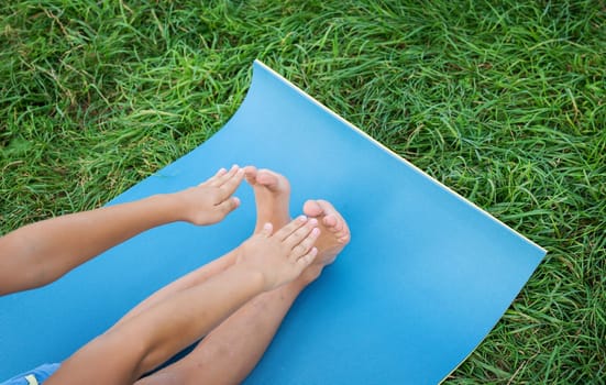 The child does exercises on a blue karemat, stretches on a rug on the grass