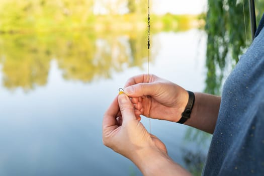 The concept of bait for fish. Close-up of a fisherman's male hand stringing bait on a fishing rod against a blue lake