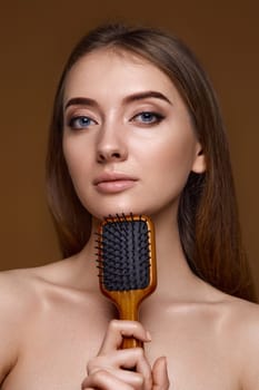 Beautiful brunette woman showing wooden brush and recommend haircare product for healthy long hair isolated on beige background