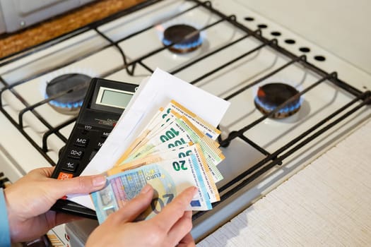Payment of utility bills, calculations on a calculator. Euro and dollar bills lie near a burning gas burner. The concept of increasing the cost of natural gas supply and payment. Energy crisis, top view