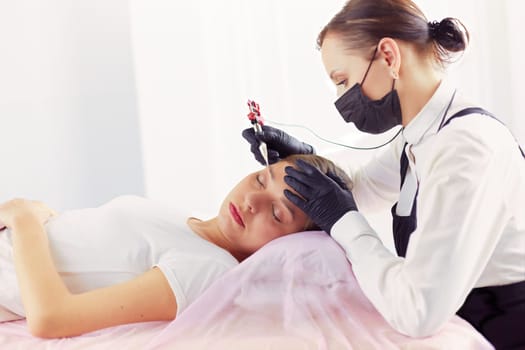 Young woman undergoing procedure of eyebrow permanent makeup in beauty salon.