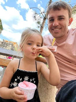 Dad and little girl eat ice cream with scoops from cups. High quality photo
