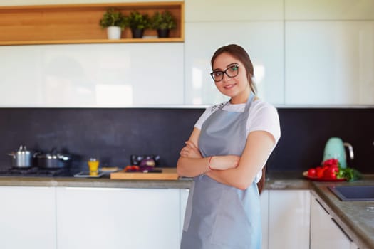 Portrait of young woman standing with arms crossed against kitchen background.
