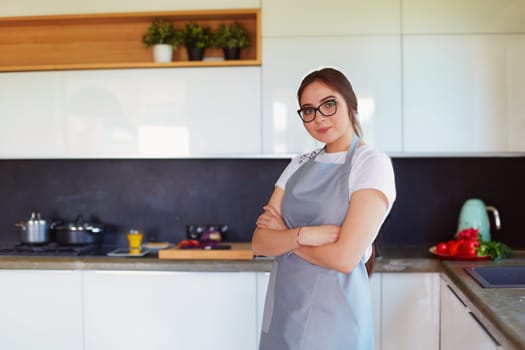 Portrait of young woman standing with arms crossed against kitchen background.