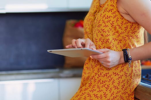 Portrait of young attractive caucasian brunette housewife at kitchen. Morning with cup of coffee and tablet pc.