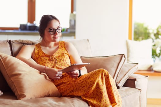 Beautiful young woman using tablet sitting on sofa at home at living room.