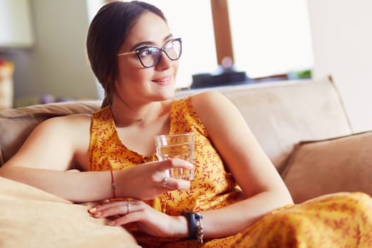 Girl drinking water sitting on a couch at home .