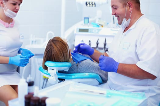 Senior male dentist in dental office talking with female patient and preparing for treatment.