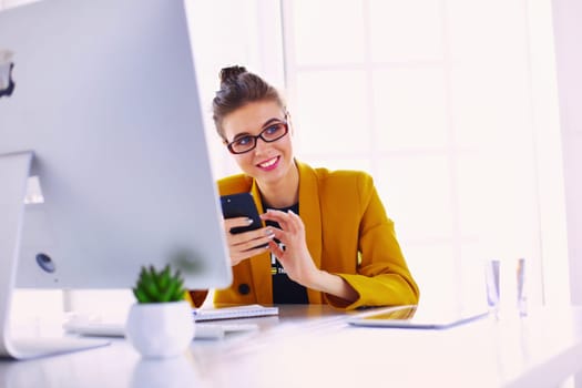 Businesswoman sitting in office with laptop on telephone.