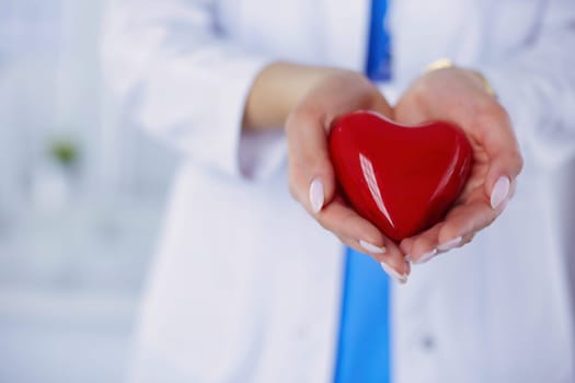 Female doctor with stethoscope holding heart, on light background.