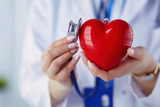 A doctor with stethoscope examining red heart, isolated on white background.