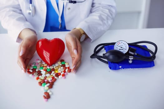 Cardiologist with red heart and stethoscope at table.