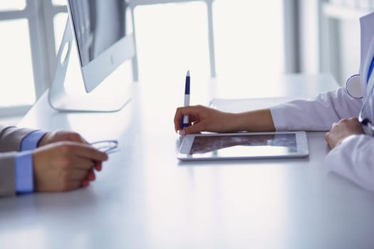 Portrait of middle aged female doctor using digital tablet while sitting at exam room and working.