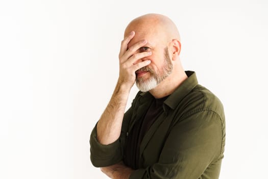 Mature man with silver beard in moment of frustration or disbelief. He puts hand on face in facepalm gesture, conveying sense of sarcasm and exasperation. White background adds emphasis to reaction. High quality photo