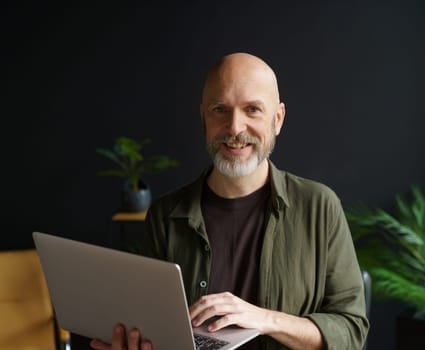Happy senior man with warm smile, holding laptop in hands home. Man's cheerful and joyful expression, highlighting his contentment and happiness. . High quality photo