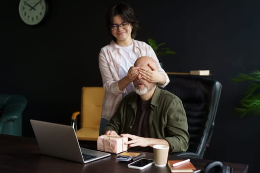 Teenager daughter and her hardworking father. Father focuses on work at computer in home office, his daughter has taken the time and effort to create special gift for him. . High quality photo