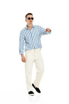 Smiling happy confident man in sunglasses and blue striped shirt standing isolated on white background. full length. Summer fashion