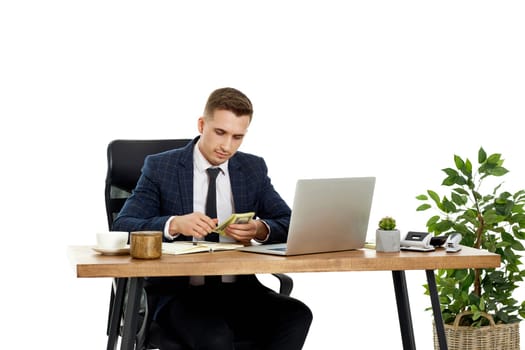 young businessman working on laptop and holding money while sitting on chair at desk.