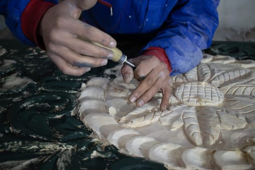 Close Up of Man Hands carving on wooden furniture. Carpenter using tool making Artistic Wood Carving. Producing an Ornament on Wood with Chisel and Hammer on a Panel of Wood . High quality photo
