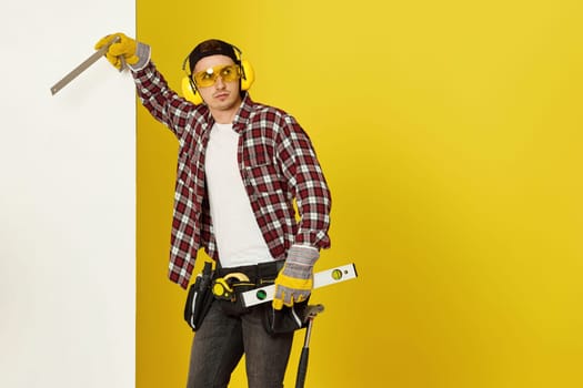 Worker man or builder in construction helmet near white banner on yellow background. building carpentry profession