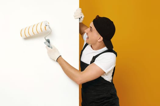 worker handyman in working clothes painting white walls in the room. copy space for text