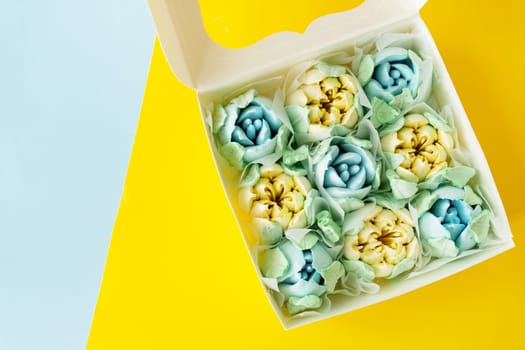 Yellow-blue marshmallow in the form of flowers in the form of tulips. Marshmallow in a box on a yellow-blue background. View from above