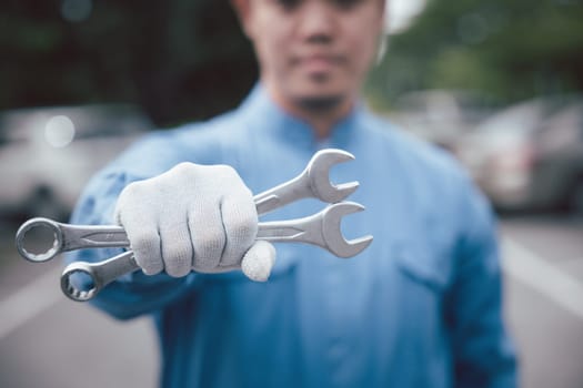 Skilled car mechanic at work, wearing a blue uniform and holding a large wrench while repairing a vehicle on the road. Close-up shot of hands.
