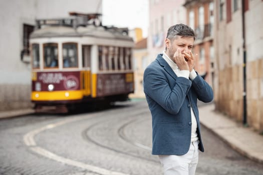 An adult man plays the harmonica on the street with a tram behind his back. Mid shot