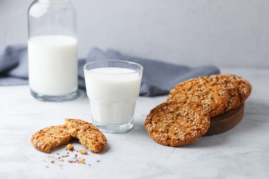 Oatmeal cookies with sesame seeds and flax seeds with a glass of milk on a gray background.