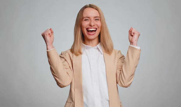 Happy joyful office business woman shouting, raising fists in gesture I did it, celebrating success, winning, birthday, lottery jackpot goal achievemen, good news. Adult girl on gray studio background