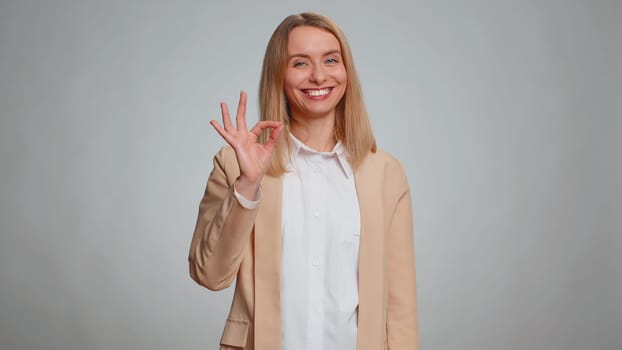 Ok. Joyful happy office woman in suit looking approvingly at camera showing approve feedback gesture like sign positive something good. Business girl alone on gray background. People sincere emotion