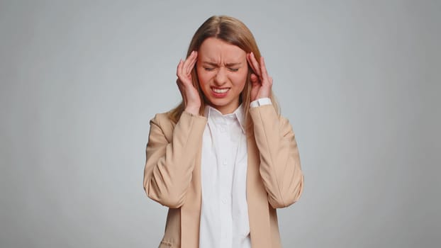 Business woman in formal office suit rubbing temples to cure headache problem, suffering from tension, migaine, stress, grimacing in pain, high blood pressure isolated alone on gray wall background