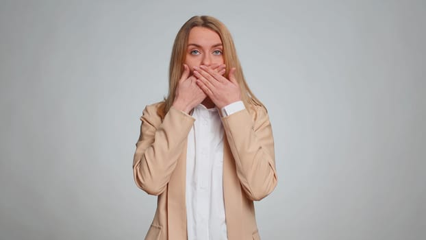 I will not say anyone any word. Frightened woman closing mouth with hands looking intimidated scared at camera gestures no refusing to tell terrible secret, unbelievable truth. Girl on gray background