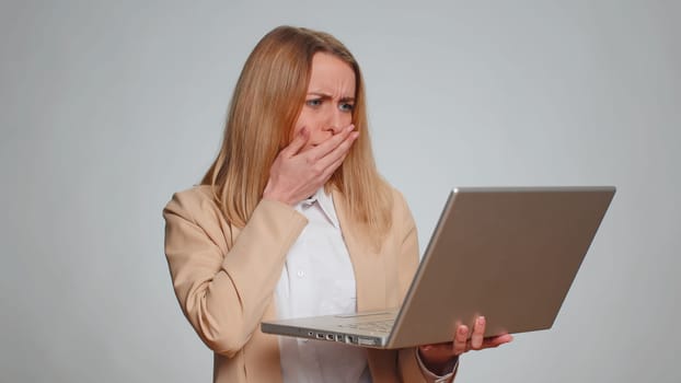 Portrait of young businesswoman use laptop typing browsing working, loses becoming surprised sudden lottery results, bad news, fortune loss, fail. Female girl in formal suit. Woman on gray background