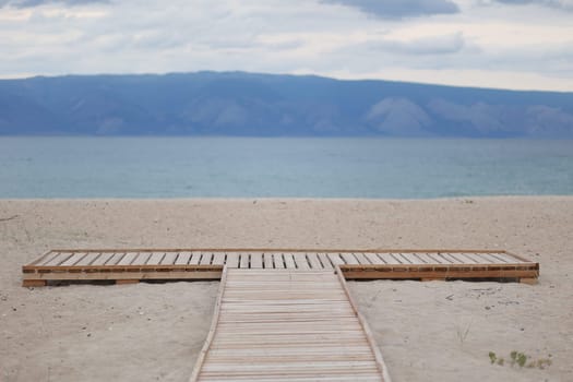 A wooden platform on the white sand of the Baikal coast on Olkhon Island against a beautiful backdrop of mountains