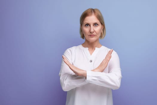 serious blond middle aged woman in white blouse with hand cross gesture on studio background.