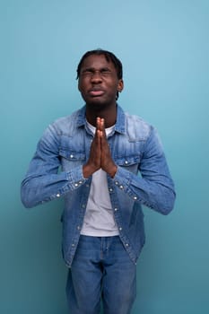 portrait of a young cheerful american man with dreadlocks in a denim jacket praying.