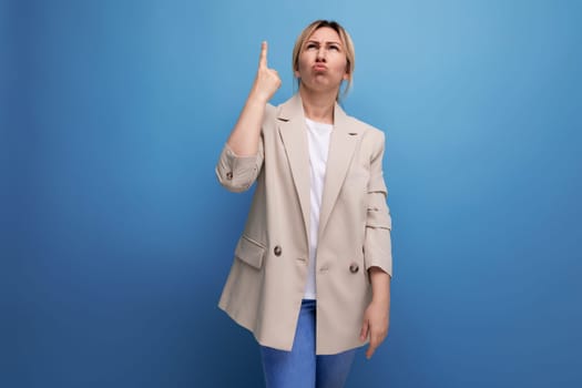 portrait of pensive european blonde 30s business woman with thumbs up on studio background.