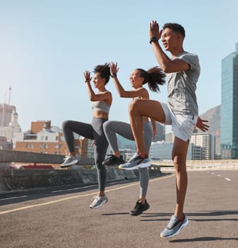 Exercise, friends and jump training in city for health, wellness and fitness. Sports, people and teamwork of runner group in street exercising, workout and jumping practice outdoors on urban road