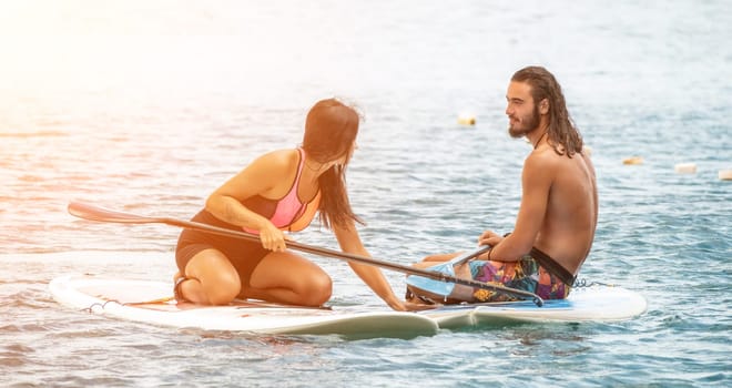 Sea woman and man on sup. Silhouette of happy young woman and man, surfing on SUP board, confident paddling through water surface. Idyllic sunset. Active lifestyle at sea or river
